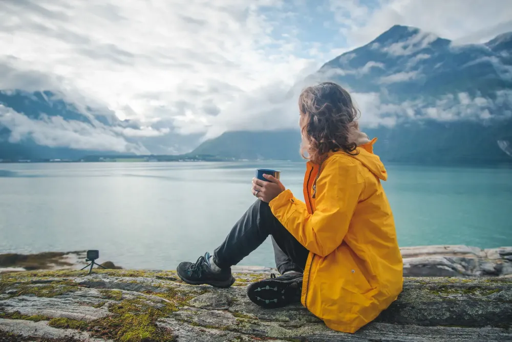 Woman drinking from mug and looking out on fjord